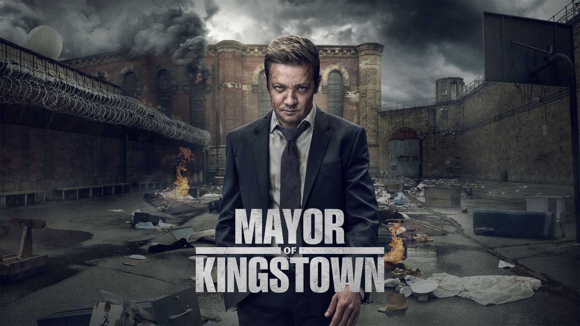 Póster de “Mayor of Kingstown” con el protagonista Mike McLusky (Jeremy Renner) en primer plano con una expresión intensa frente al paisaje urbano y penitenciario de Kingstown, con el título destacado.
