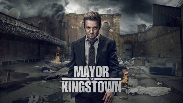 Póster de “Mayor of Kingstown” con el protagonista Mike McLusky (Jeremy Renner) en primer plano con una expresión intensa frente al paisaje urbano y penitenciario de Kingstown, con el título destacado.